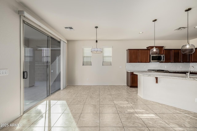 kitchen with pendant lighting, a kitchen bar, tasteful backsplash, sink, and light tile patterned floors