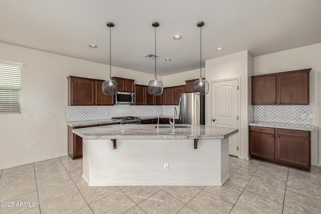 kitchen featuring hanging light fixtures, appliances with stainless steel finishes, a breakfast bar, and a kitchen island with sink