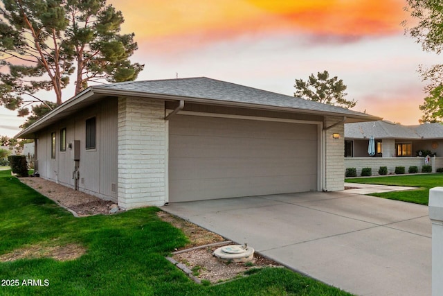 view of side of property with a garage, driveway, roof with shingles, a yard, and brick siding