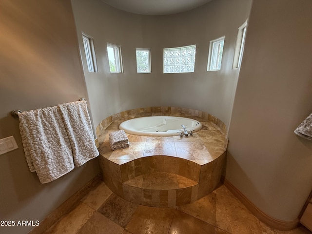 bathroom featuring baseboards, stone tile flooring, and a whirlpool tub