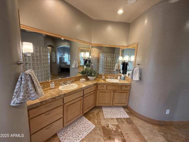 ensuite bathroom featuring ensuite bath, double vanity, baseboards, and a sink