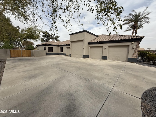 view of side of home featuring stucco siding, fence, concrete driveway, an attached garage, and a tiled roof