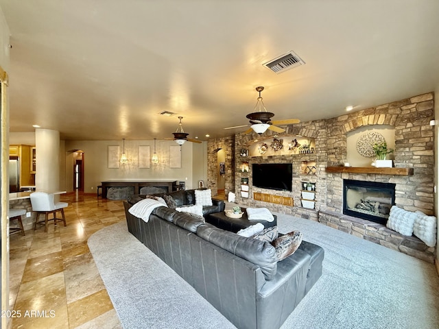 living area with visible vents, ceiling fan, a fireplace, and stone finish flooring