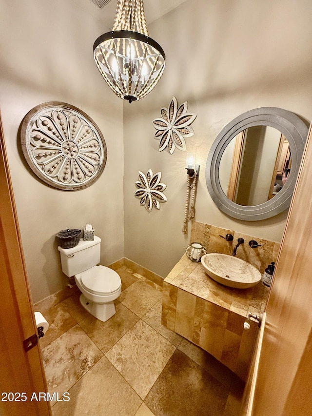 bathroom featuring an inviting chandelier, toilet, baseboards, and a sink