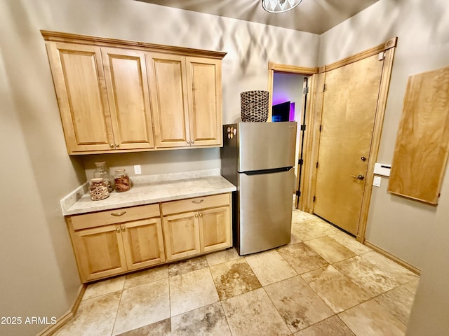 kitchen with a baseboard heating unit, light brown cabinets, and freestanding refrigerator