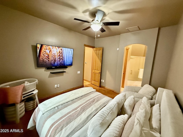 bedroom with a ceiling fan, ensuite bathroom, wood finished floors, arched walkways, and baseboards