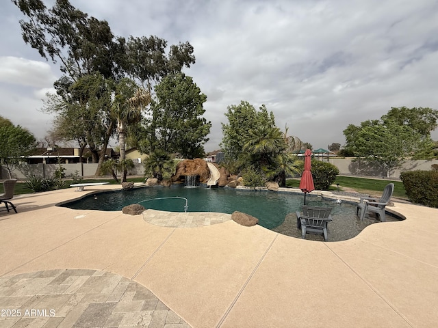 pool with a patio area, a diving board, a water slide, and fence