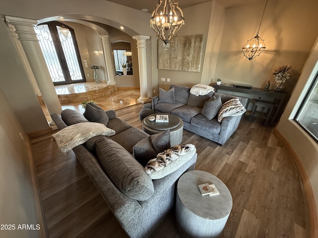 living area featuring a notable chandelier, wood finished floors, french doors, arched walkways, and decorative columns