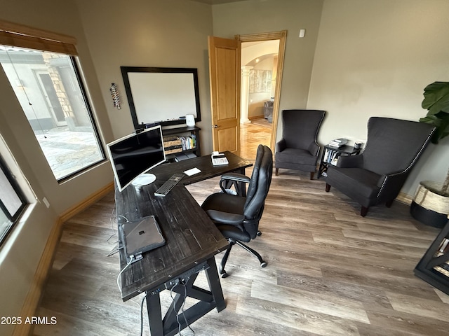 office space featuring baseboards, arched walkways, and wood finished floors