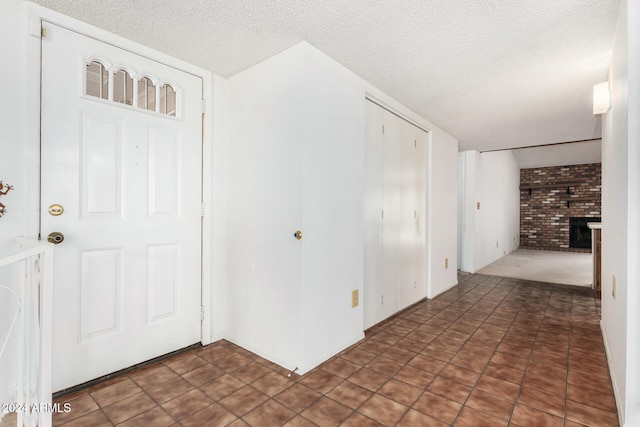 entryway featuring brick wall, a fireplace, a textured ceiling, and dark tile patterned flooring