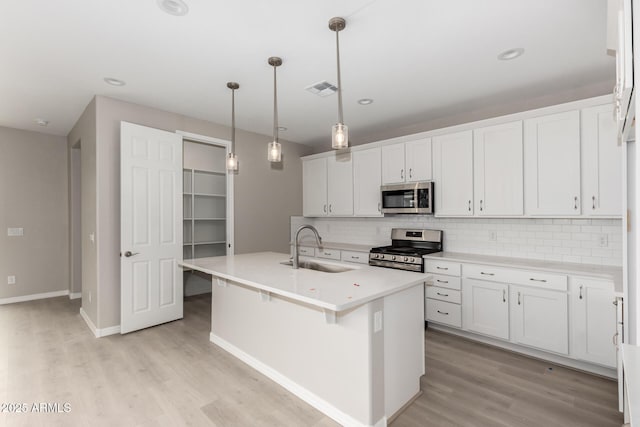 kitchen with appliances with stainless steel finishes, sink, pendant lighting, a center island with sink, and white cabinets