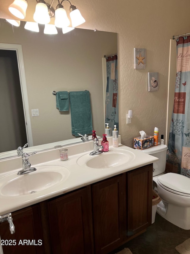 bathroom featuring a textured wall, double vanity, a sink, and toilet