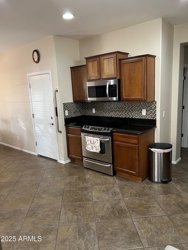 kitchen with brown cabinets, stainless steel appliances, dark countertops, tasteful backsplash, and baseboards