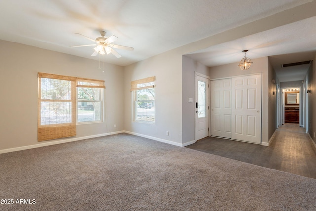 empty room featuring dark colored carpet, baseboards, visible vents, and ceiling fan