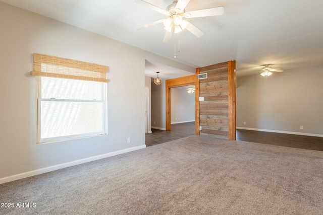 unfurnished room featuring visible vents, ceiling fan, dark colored carpet, wooden walls, and baseboards