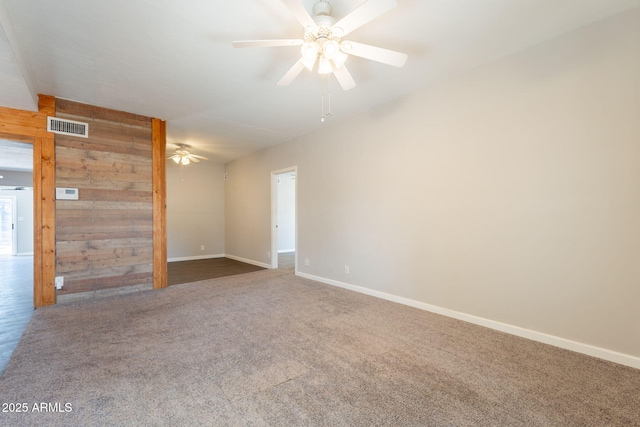 empty room with baseboards, carpet flooring, ceiling fan, visible vents, and wooden walls