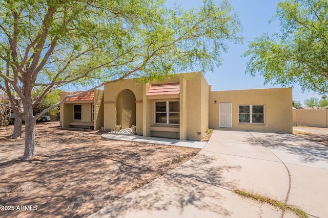 pueblo-style house with concrete driveway, stucco siding, and fence