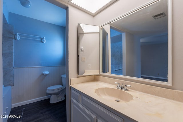 bathroom with toilet, visible vents, vanity, a wainscoted wall, and wood finished floors