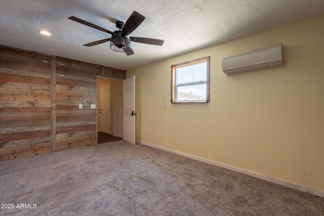 carpeted spare room with baseboards, wood walls, a wall mounted air conditioner, and ceiling fan