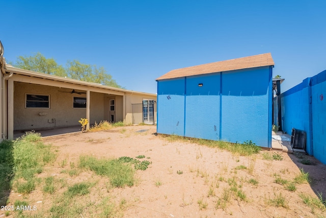 rear view of property featuring an outdoor structure, stucco siding, ceiling fan, and a storage shed