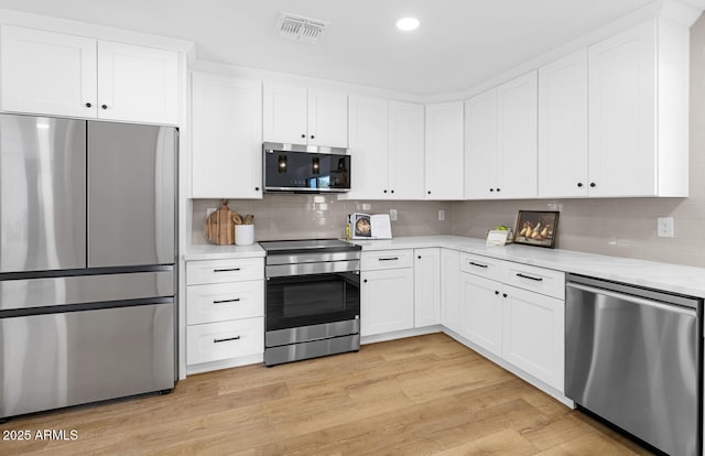 kitchen featuring white cabinetry, stainless steel appliances, backsplash, and light wood-type flooring