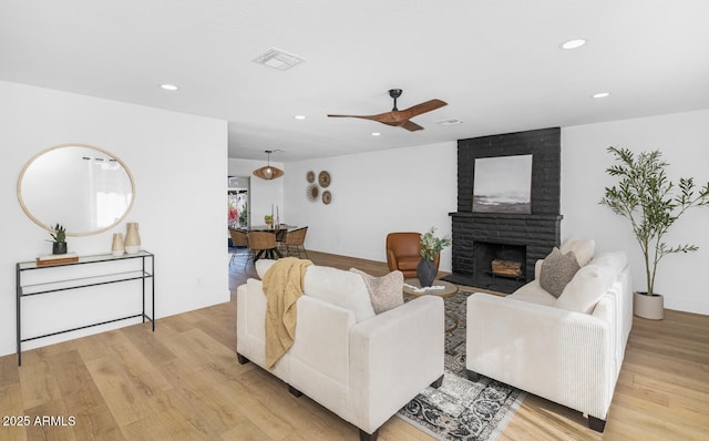 living room with ceiling fan, light hardwood / wood-style floors, and a brick fireplace