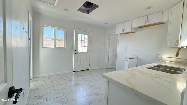 kitchen with light stone countertops, sink, and white cabinetry