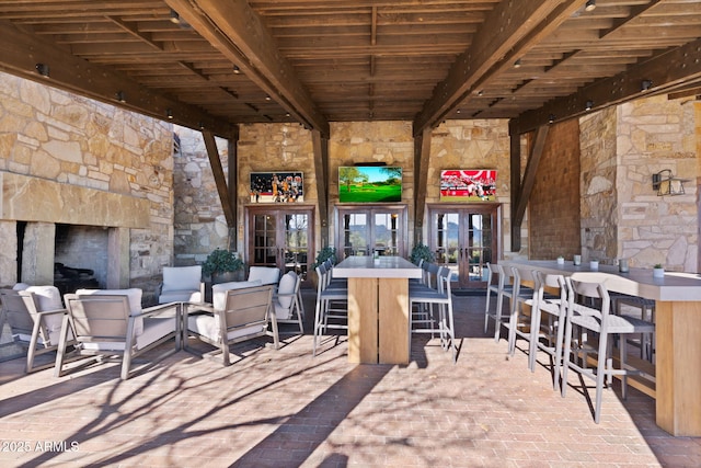 view of patio / terrace featuring a bar, french doors, and an outdoor stone fireplace