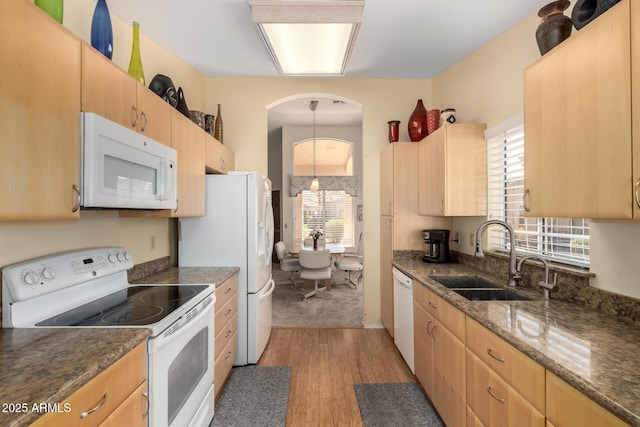 kitchen with light wood-type flooring, light brown cabinets, a sink, dark stone countertops, and white appliances