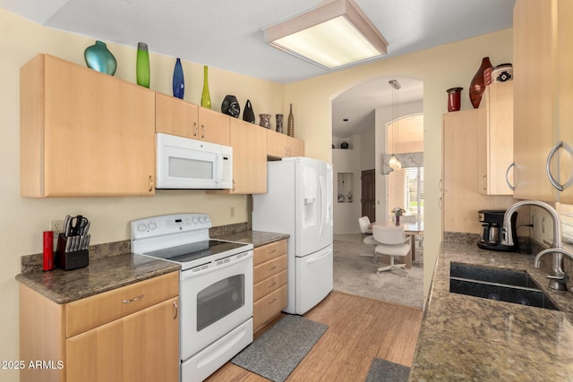 kitchen with dark countertops, light brown cabinets, light wood-type flooring, white appliances, and a sink