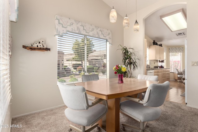 dining area featuring arched walkways, visible vents, light colored carpet, and lofted ceiling