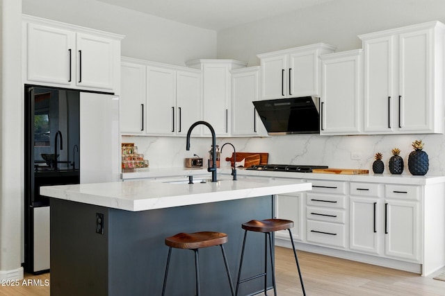 12428 S 179th Ln, Goodyear, AZ 85338 - kitchen featuring exhaust hood, light wood-style flooring, white cabinets, backsplash, and a center island with sink