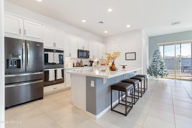 kitchen featuring a kitchen breakfast bar, stainless steel appliances, a center island, light tile patterned floors, and white cabinetry