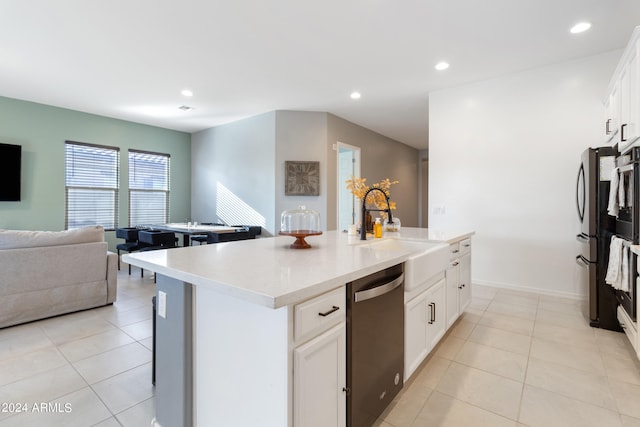 kitchen featuring white cabinets, light tile patterned floors, a kitchen island with sink, dishwasher, and sink