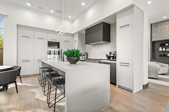 kitchen with decorative light fixtures, light hardwood / wood-style floors, oven, a kitchen island with sink, and a breakfast bar area