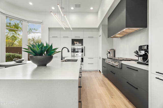 kitchen with wall chimney exhaust hood, hanging light fixtures, a spacious island, stainless steel gas stovetop, and sink