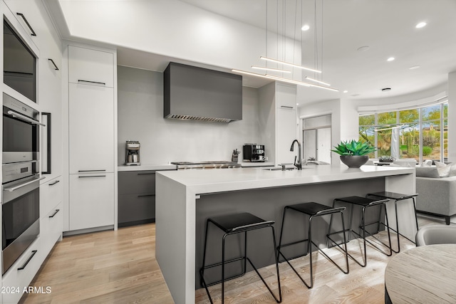 kitchen with light hardwood / wood-style floors, hanging light fixtures, white cabinetry, and a center island with sink