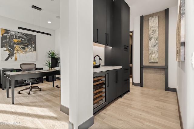 bar featuring sink, beverage cooler, light wood-type flooring, and hanging light fixtures