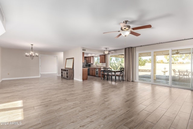 unfurnished living room with ceiling fan with notable chandelier and light hardwood / wood-style flooring