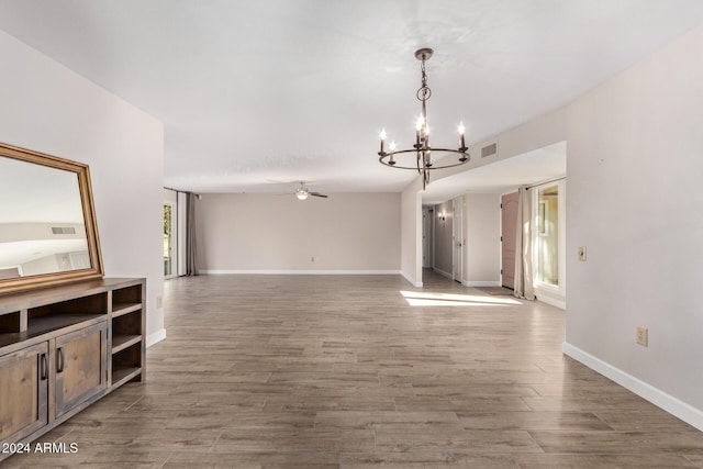 unfurnished living room featuring hardwood / wood-style flooring, ceiling fan with notable chandelier, and a wealth of natural light