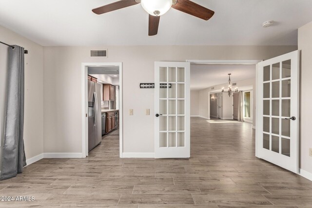 unfurnished room with ceiling fan with notable chandelier, wood-type flooring, and french doors