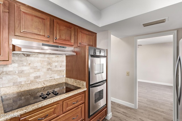 kitchen with backsplash, light hardwood / wood-style floors, light stone counters, and stainless steel appliances