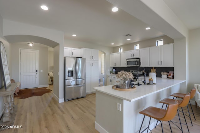 kitchen with arched walkways, backsplash, appliances with stainless steel finishes, a peninsula, and a kitchen breakfast bar