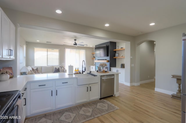 kitchen with arched walkways, light wood-style flooring, stainless steel dishwasher, white cabinetry, and a sink