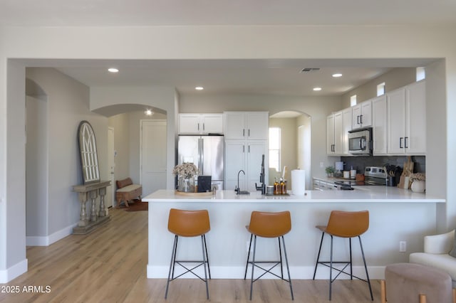 kitchen featuring arched walkways, stainless steel appliances, a breakfast bar area, and a peninsula