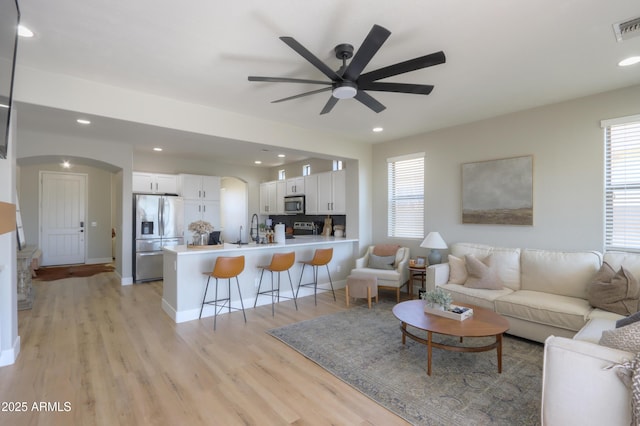 living room featuring light wood-style flooring, arched walkways, a wealth of natural light, and recessed lighting