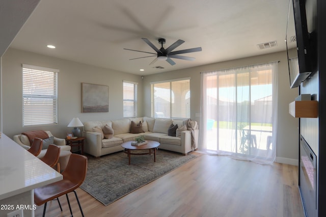 living room featuring a glass covered fireplace, visible vents, recessed lighting, and wood finished floors