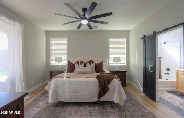 bedroom featuring a barn door, light wood-style flooring, visible vents, baseboards, and ensuite bath