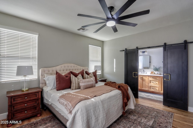 bedroom featuring light wood-style floors, visible vents, multiple windows, and a barn door