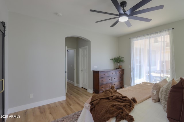 bedroom with arched walkways, a barn door, a ceiling fan, wood finished floors, and baseboards